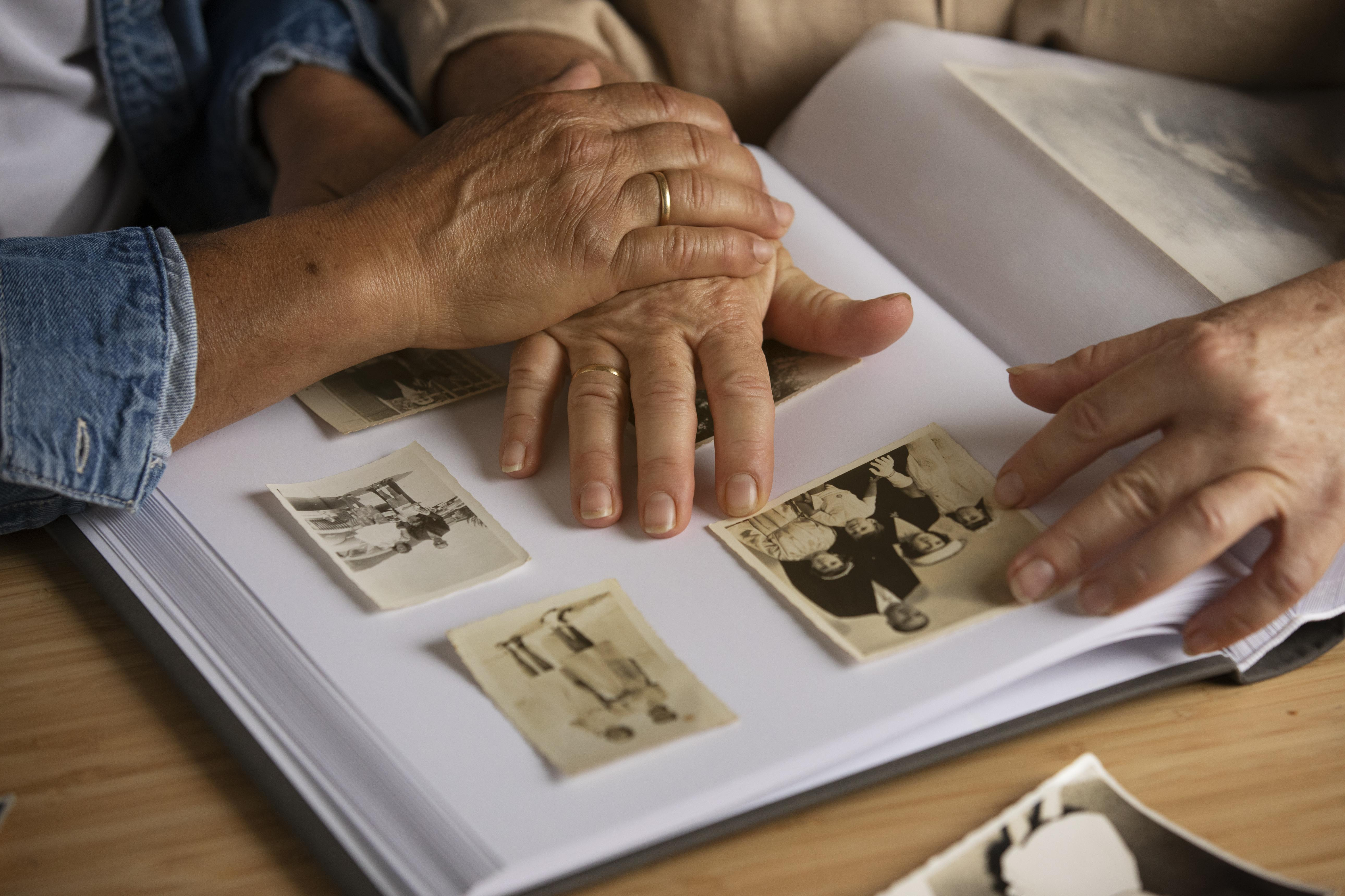 Manos de una persona mayor y una cuidadora sobre un álbum de fotos antiguas, representando el duelo anticipado en el Alzheimer